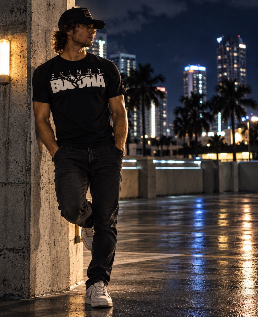 Skinnybuddha Classic black logo T-shirt styled with dark jeans against a night city backdrop